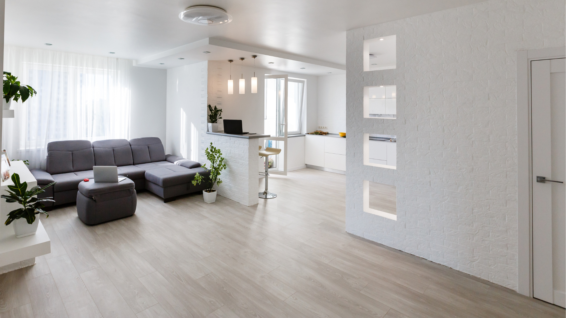 Same room after renovation — finished living space with sectional, painted walls, hardwood floor.