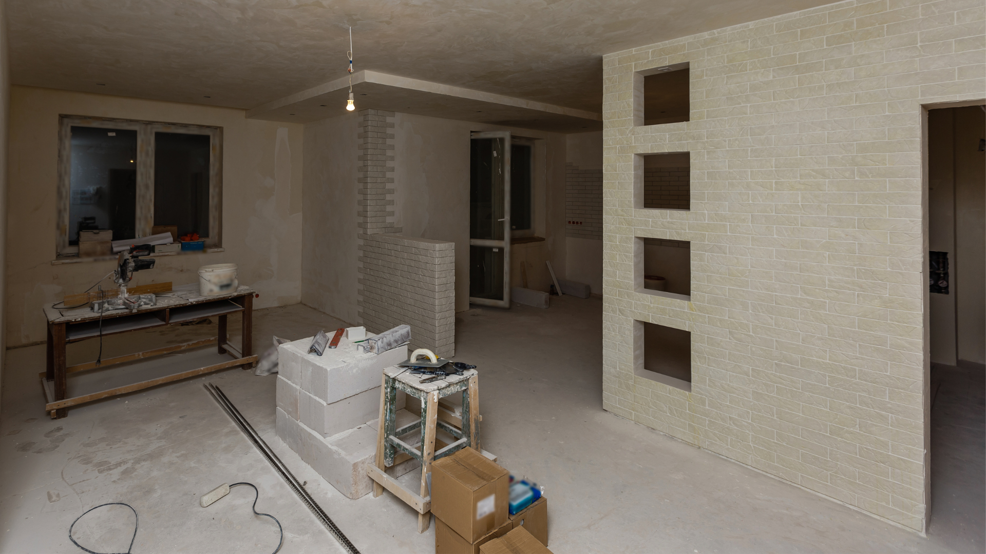 Room before renovation — bare drywall, exposed brick, construction debris.